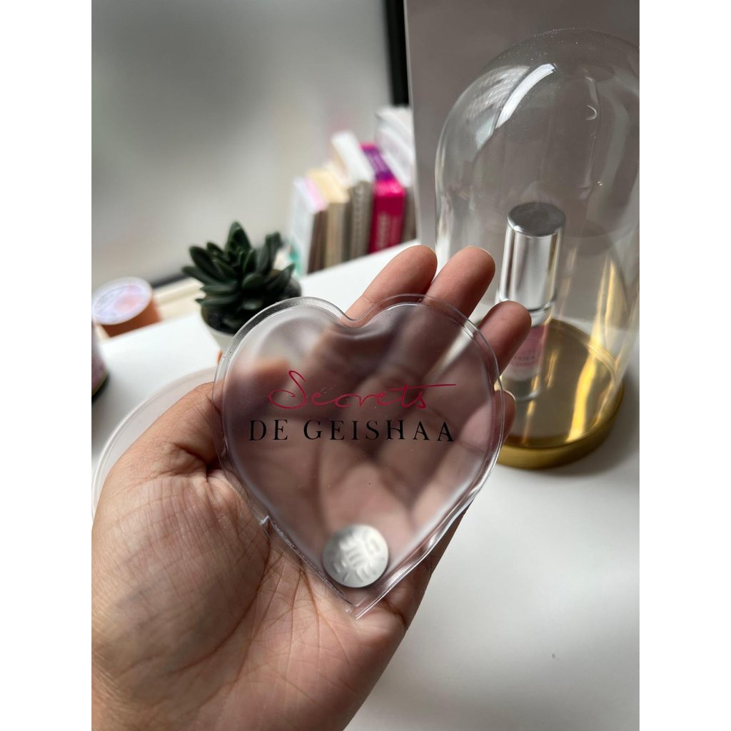Cœur chauffant transparent Secrets de Geishaa tenu dans une main, avec sa pastille métallique.